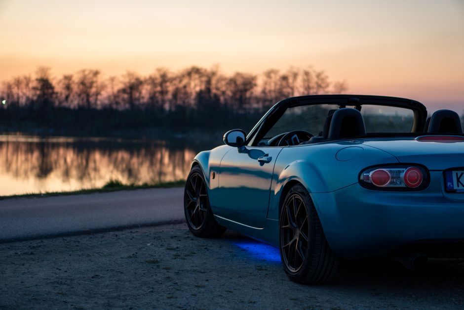 A sports car parked by a lake at sunset in Brzegi, Poland, offering a scenic view.