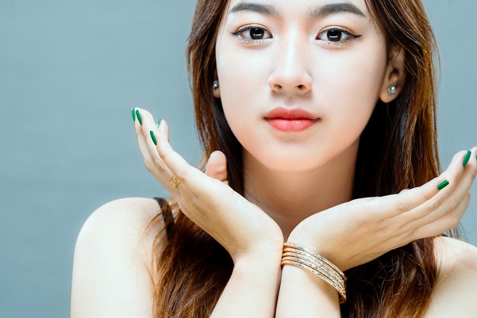 A close-up portrait showcasing a woman with long brown hair and hands under her chin against a white background.