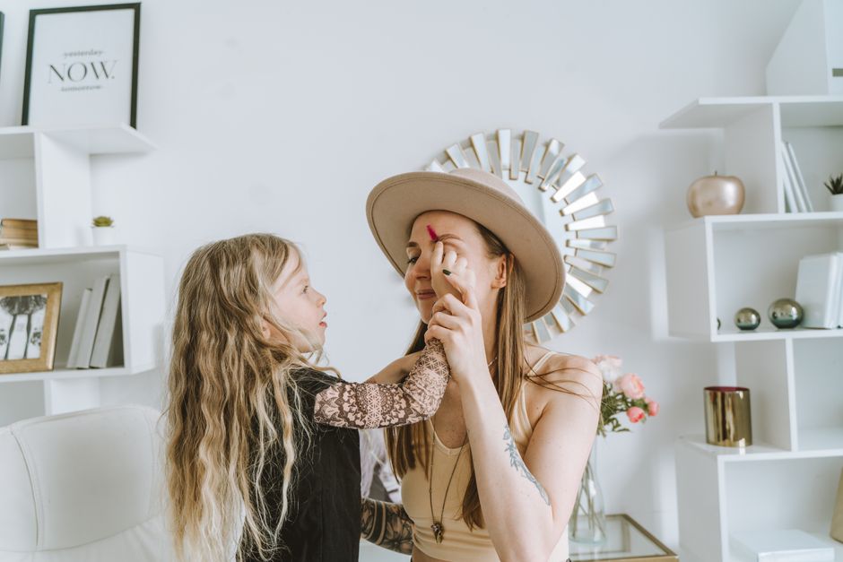 A young girl applies makeup to her mother in a cozy indoor setting, capturing a tender family moment.