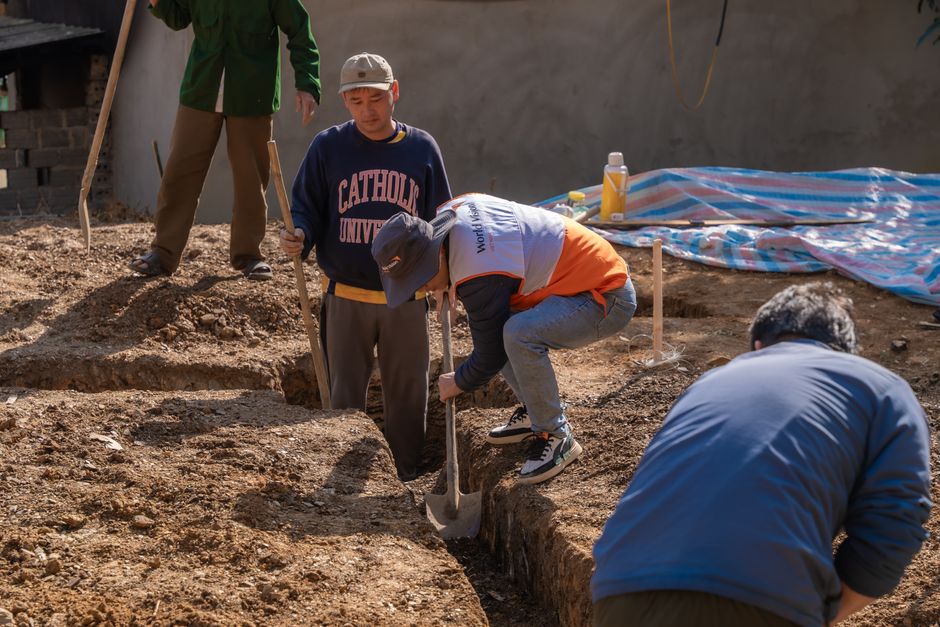 Volunteers working together to dig a trench at a construction site in daylight.