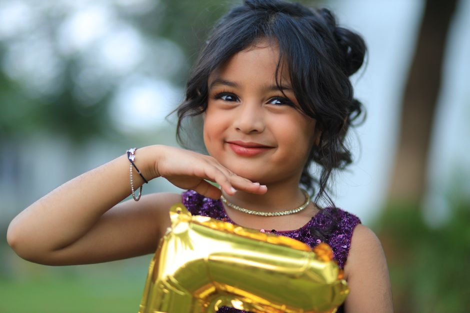 Adorable child smiling while holding a golden number balloon, outdoors in a playful setting.