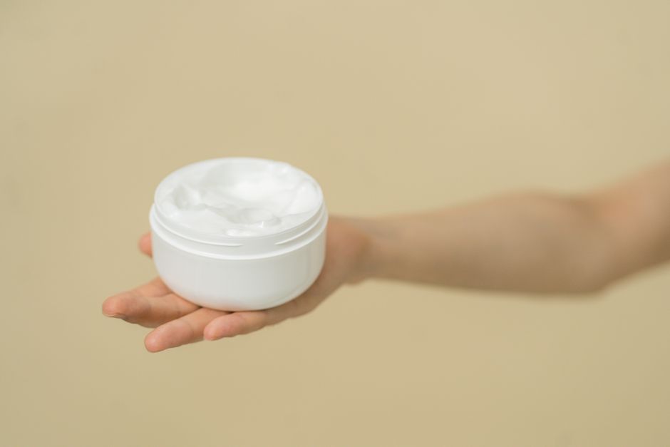 Close-up of a hand holding a white cream jar with a minimalist beige backdrop.