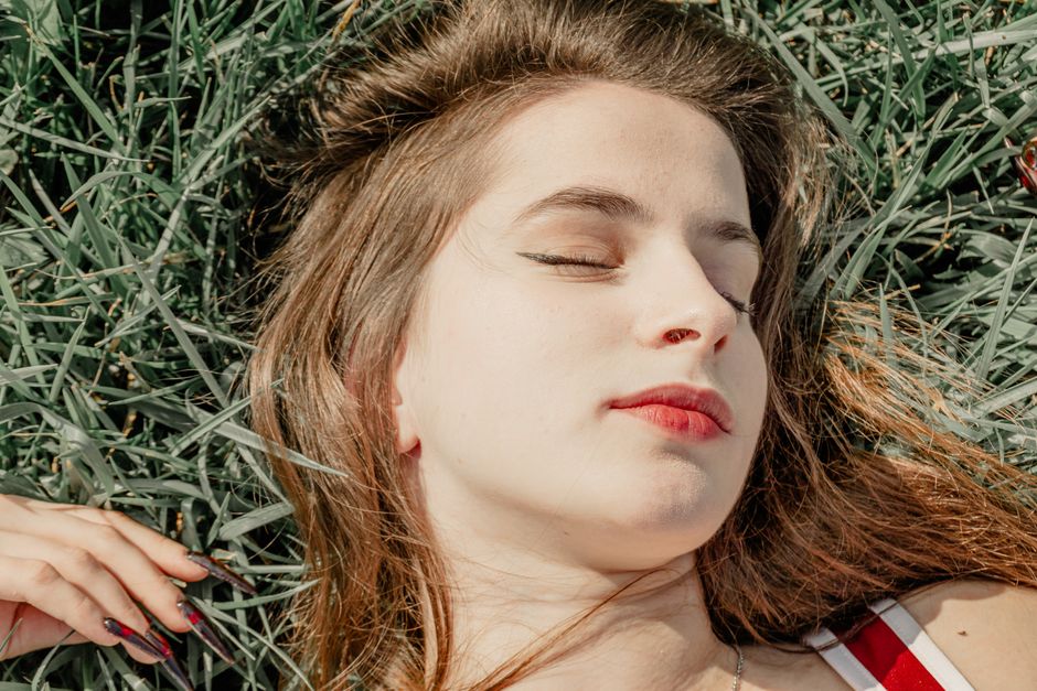 Portrait of a young woman with eyes closed lying on grass, enjoying sunlight.