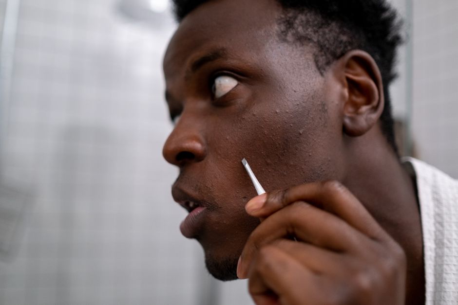 Side profile of a man using tweezers for skincare in a bathroom setting.