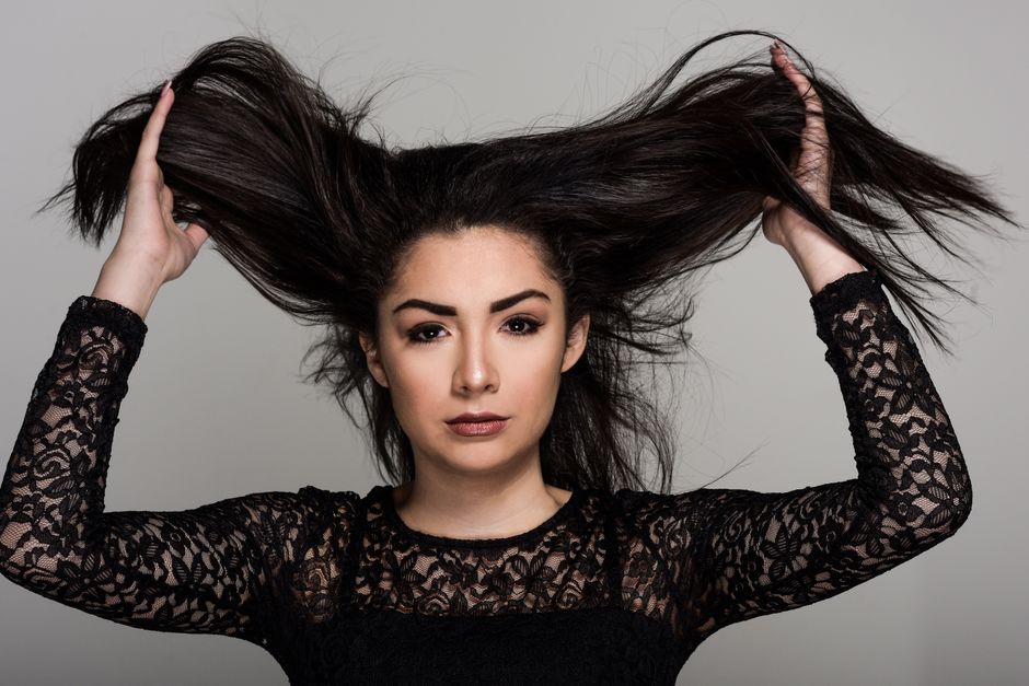 Portrait of a woman in lace attire, holding her hair up with confidence. Studio shot.