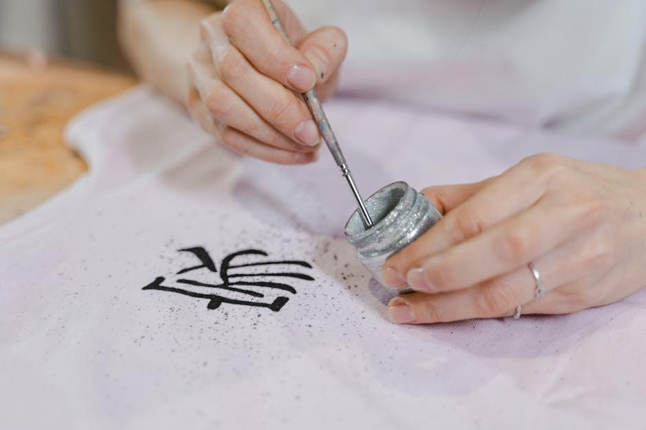 Close-up of an artisan hand painting textile with glitter and brush.
