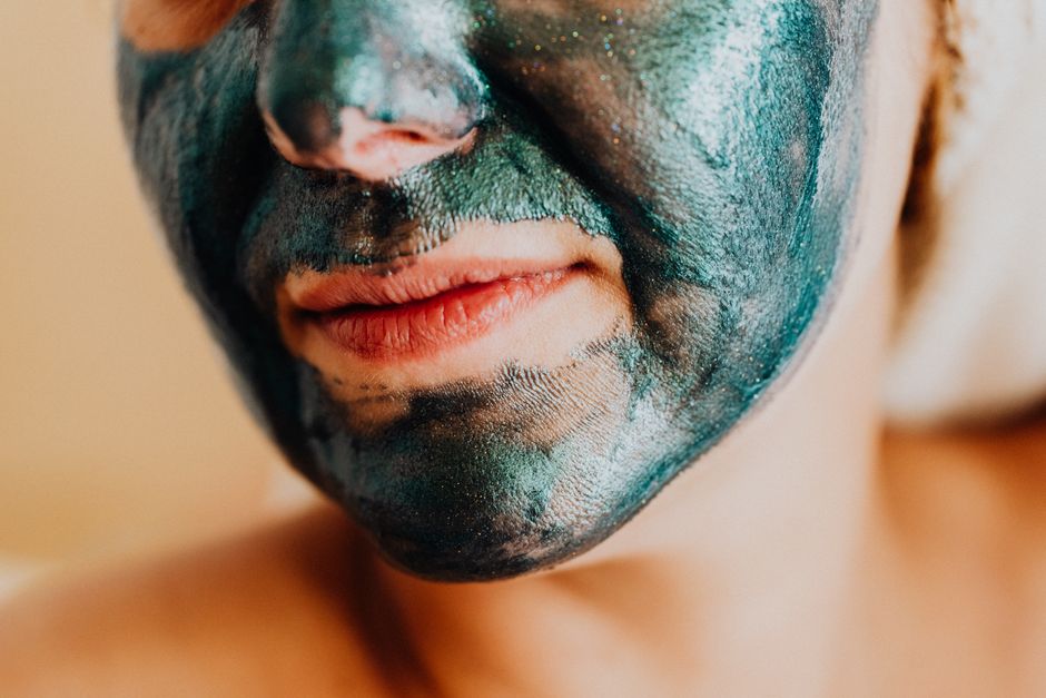 A close-up shot of a woman's face with a shimmering green facial mask for skincare.