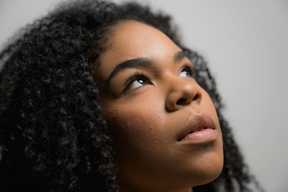 A close-up portrait of a woman with natural curly hair, looking up thoughtfully.