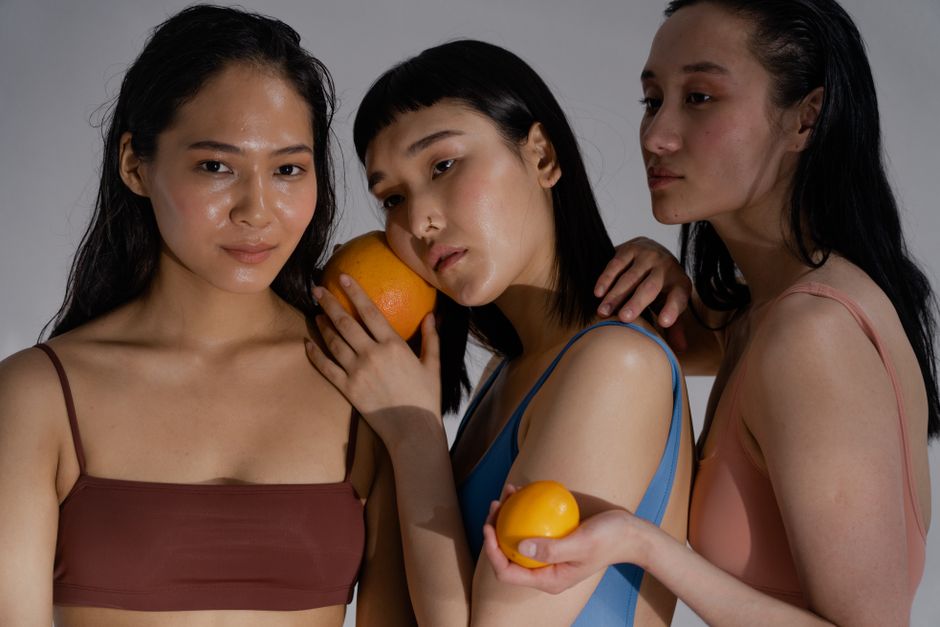 Three women in swimwear posing with oranges, embodying fresh and vibrant fashion in a studio setting.