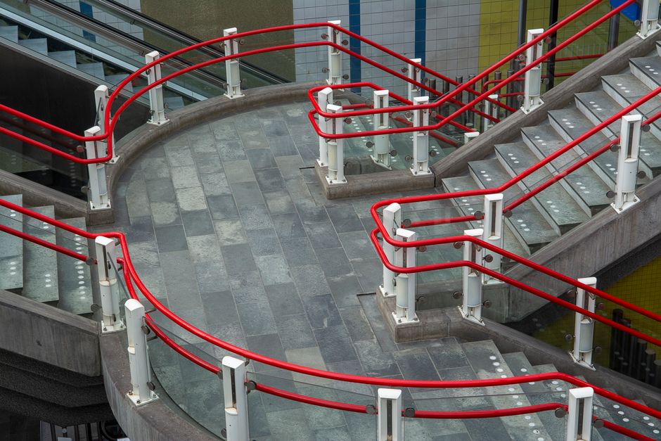 Contemporary staircase with vibrant red railings in a Rotterdam station, showcasing urban architecture.