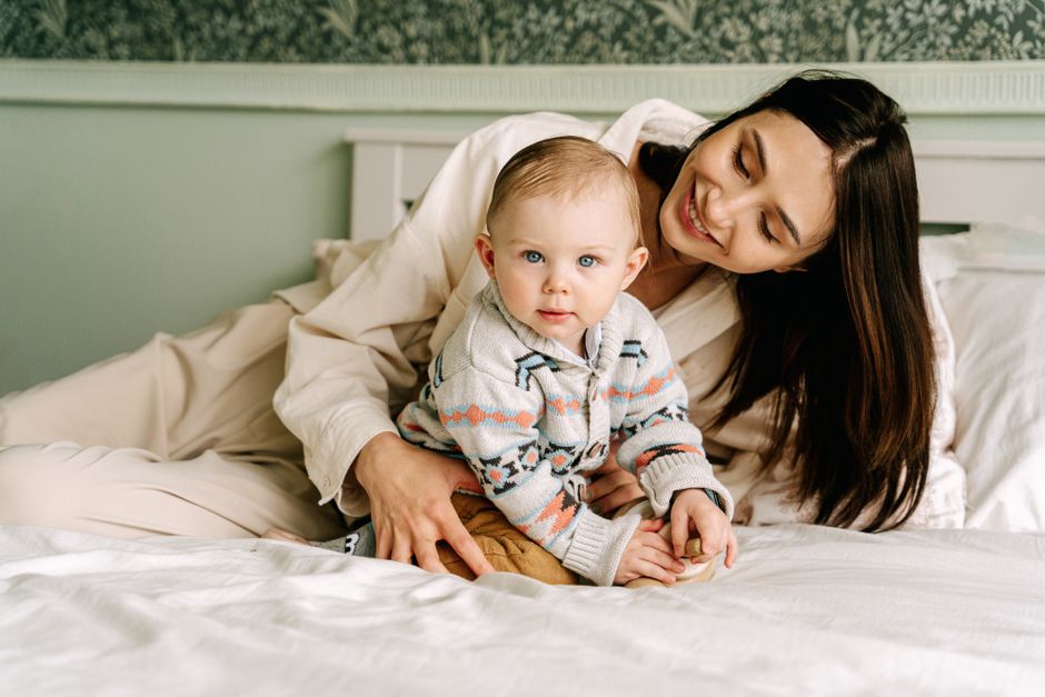 A happy mother and her baby sitting together on a bed, creating a warm family moment.