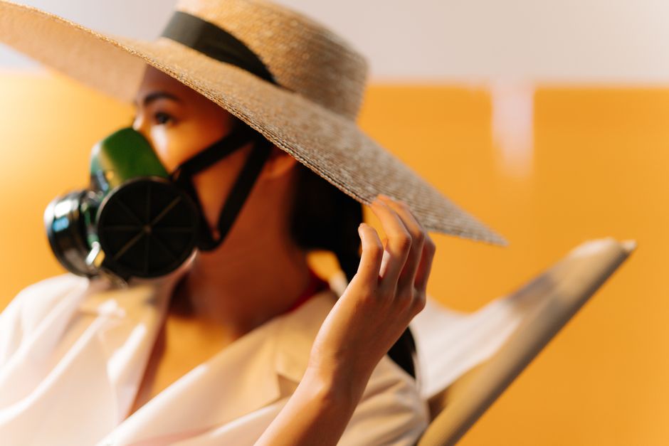 Portrait of a woman wearing a respirator and straw hat, conceptually highlighting air quality issues.