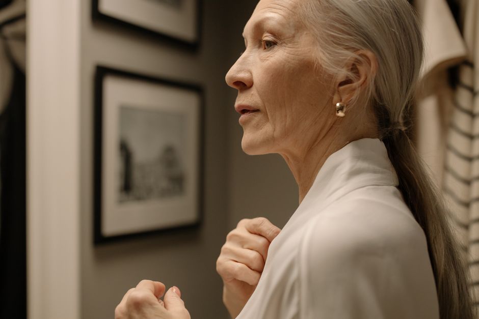 Elegant senior woman in profile wearing a robe with jewelry, in an indoor setting.