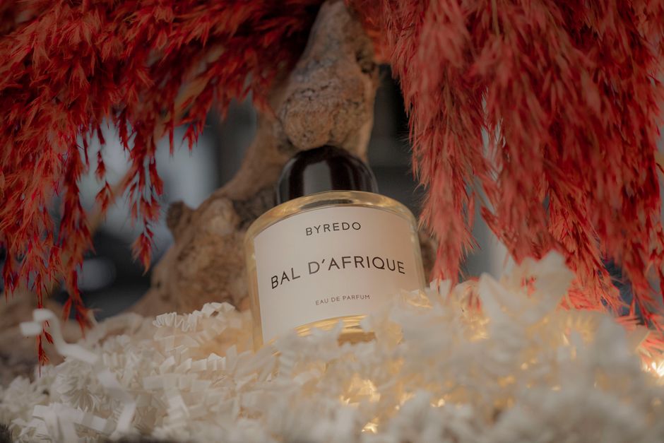 Elegant Byredo Bal D'Afrique perfume with vibrant red floral backdrop.