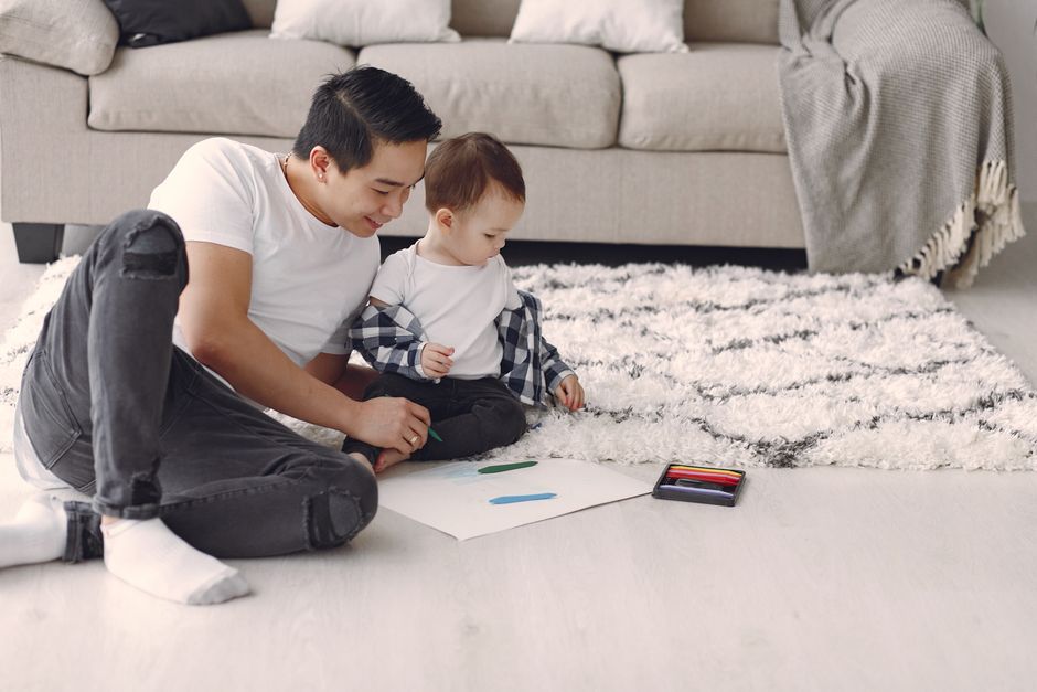 A father and son bonding over a drawing activity on the living room floor.