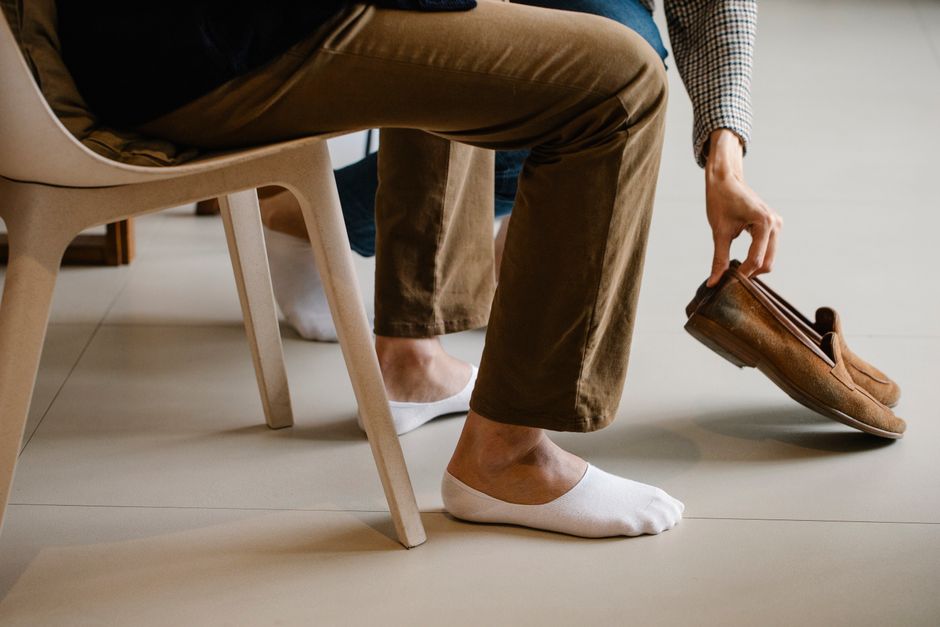 Man sitting indoors, reaching for loafers. Casual wear focus.
