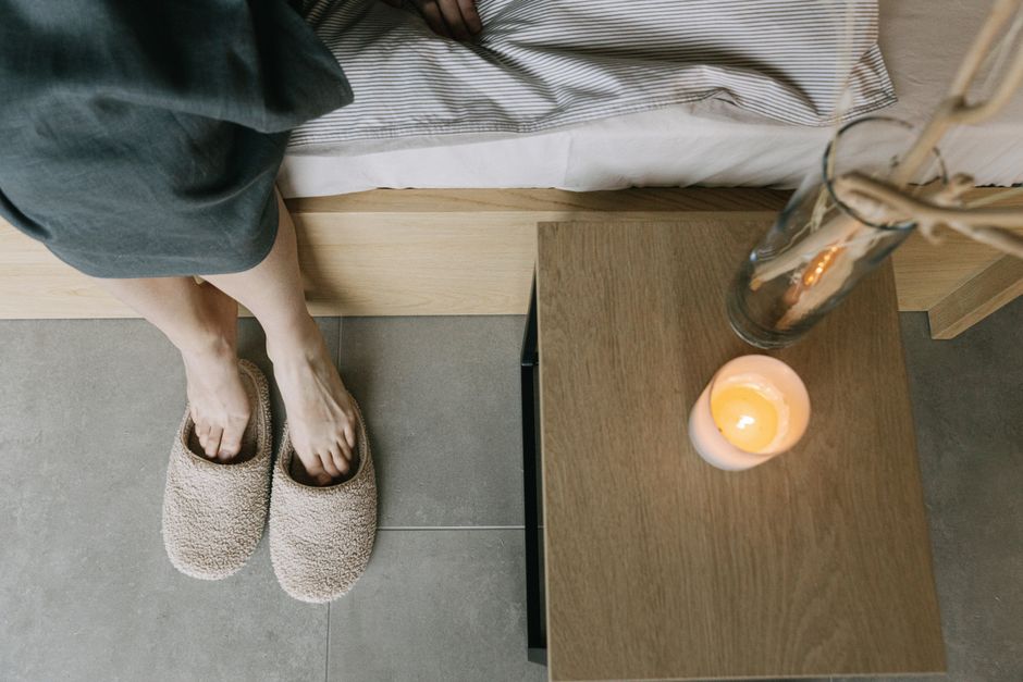 A tranquil bedroom setting featuring slippers, a wooden table, and a lit candle.