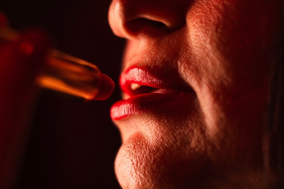 Artistic close-up of a woman's lips applying red lipstick. Dramatic lighting.