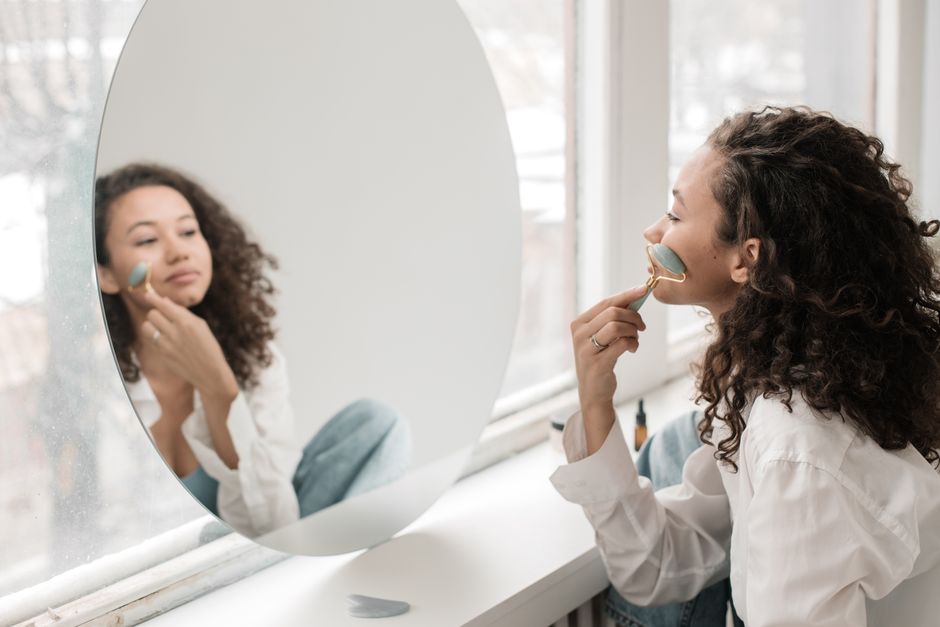 A woman practicing facial care with a jade roller in a bright, minimalist room.