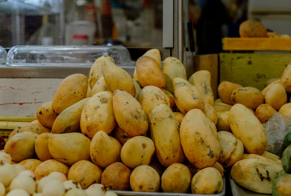 A heap of ripe yellow mangoes displayed prominently in a bustling market setting.