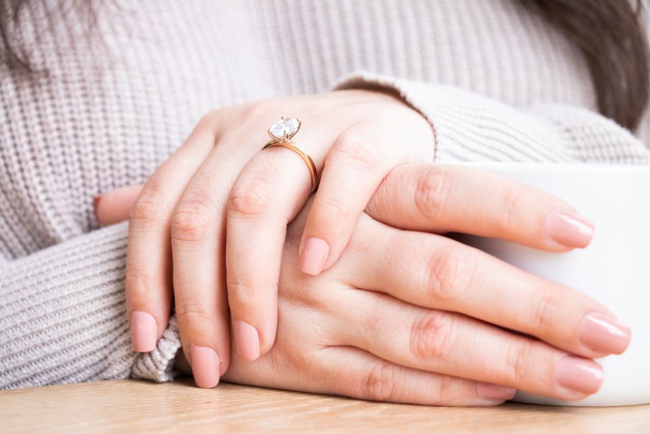 Close-up of elegant female hands with a diamond engagement ring and a coffee cup.
