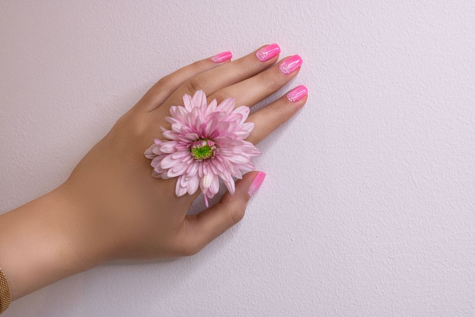 Close-up of a woman's hand with pink nails and a pink flower, showcasing delicate beauty.